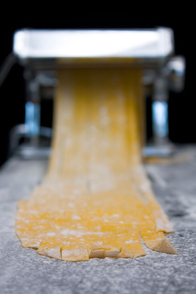 Portrait image of homemade pasta being cut with a pasta machine