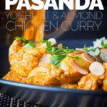 Tall close up image of a chicken pasanda curry with a pile of basmati rice and flaked almonds on a black plate with a beer in the background with text