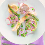 Portrait overhead image of a spring ham hock salad, featuring pressed ham hock, asparagus, peas, lettuce, radish, and puffed pork crackling with text.