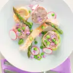 Portrait overhead image of a spring ham hock salad, featuring pressed ham hock, asparagus, peas, lettuce, radish, and puffed pork crackling with text.