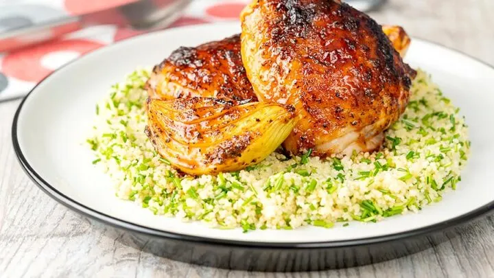 Landscape image of roasted harissa chicken thighs with onion wedges served on herbed couscous