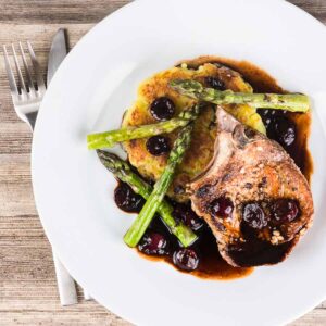 Simply pan fried pork chops are served with a simple potato rosti, some balsamic cherries and asparagus for an old school but delightful meal!