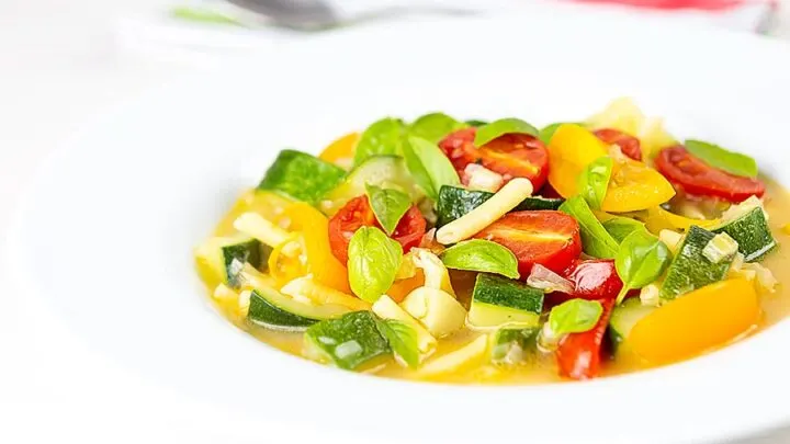 A bright and colourful summer vegetable soup served in a white bowl