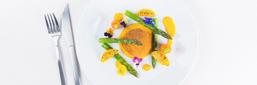 Bonbons made from confit duck legs served on a carrot puree and fresh steamed asparagus on a white plate against a bright background.