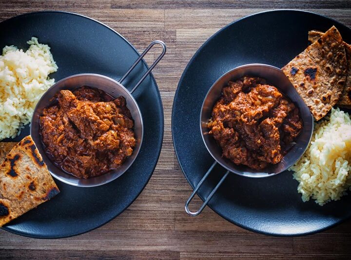 Landscape overhead image of lamb madras curry served with white rice and chapatis served on a black plate