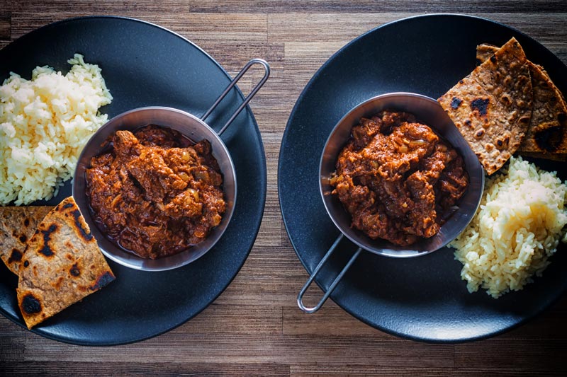 Landscape overhead image of lamb madras curry served with white rice and chapatis served on a black plate
