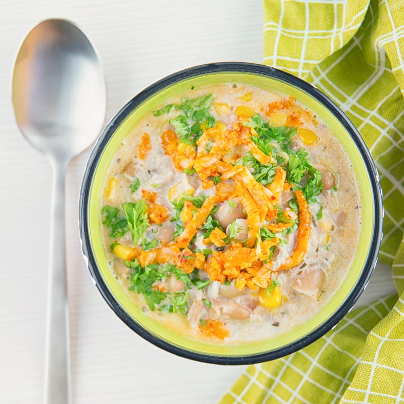 A square image taken from above of a white chili chicken topped with red Leicester cheese in a bright colourful bowl
