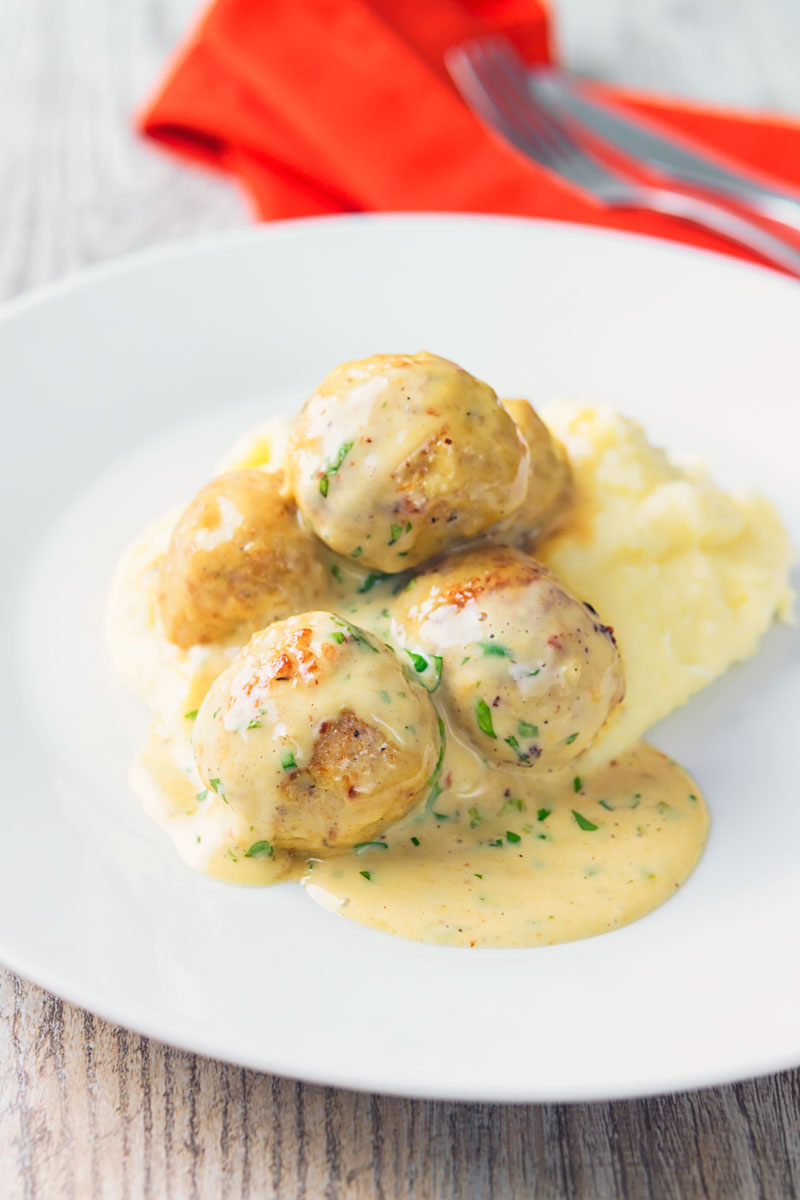 Portrait image of chicken meatballs in a honey and mustard sauce on mashed potatoes served on a white plate.