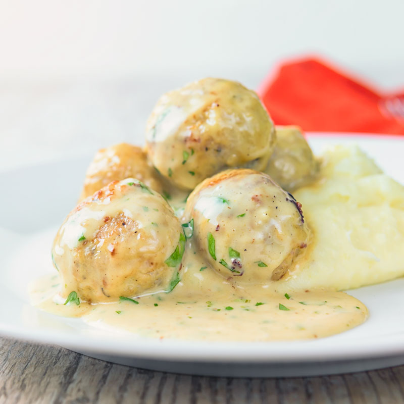 Square image of chicken meatballs in a honey and mustard sauce on mashed potatoes served on a white plate.
