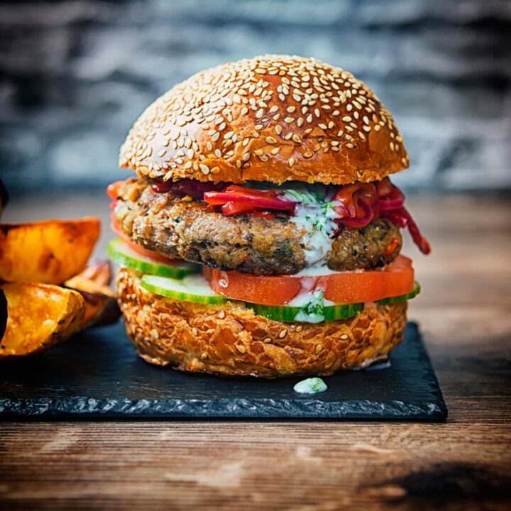 Square image of an Indian inspired spicy lamb burger with a red onion chutney served with potato wedges