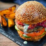 Portrait image of an Indian inspired spicy lamb burger with a red onion chutney served with potato wedges