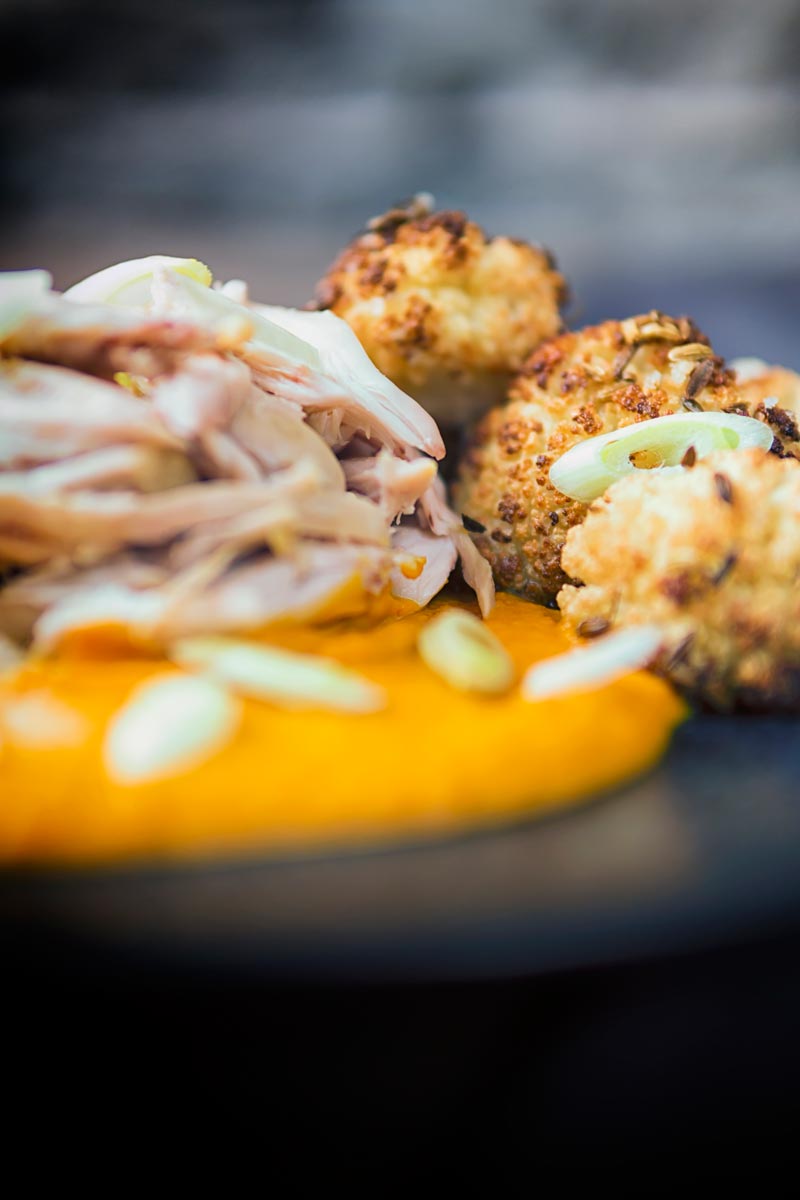 Portrait image of shredded slow cooked rabbit legs with roasted cauliflower and spiced carrot puree on a dark plate