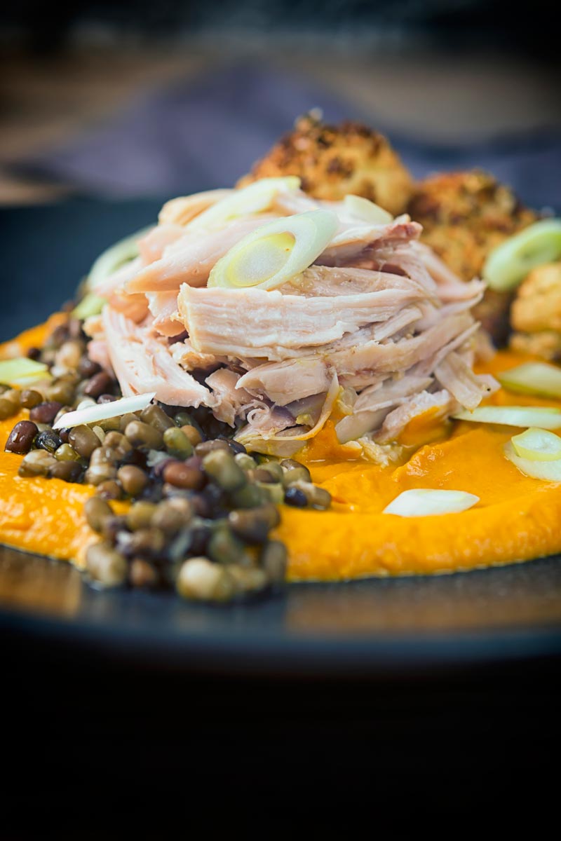Portrait image of shredded slow cooked rabbit legs with mung beans and spiced carrot puree on a dark plate
