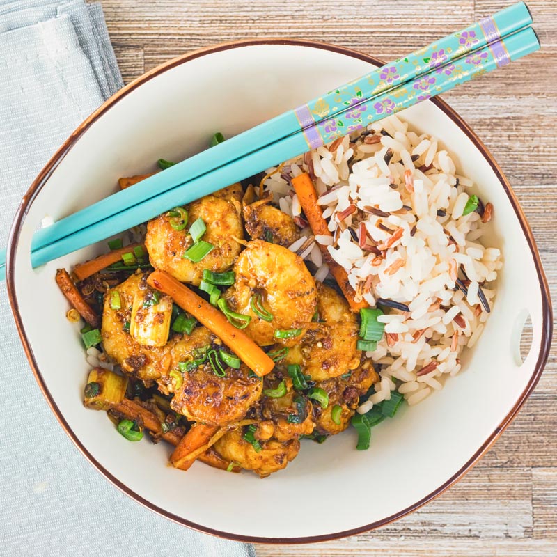 Square overhead image of shrimp stir fry in an Asian style bowl with a blue flower