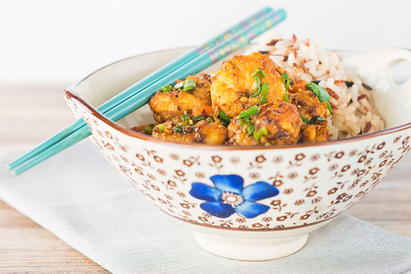 Landscape image of shrimp stir fry in an Asian style bowl with a blue flower