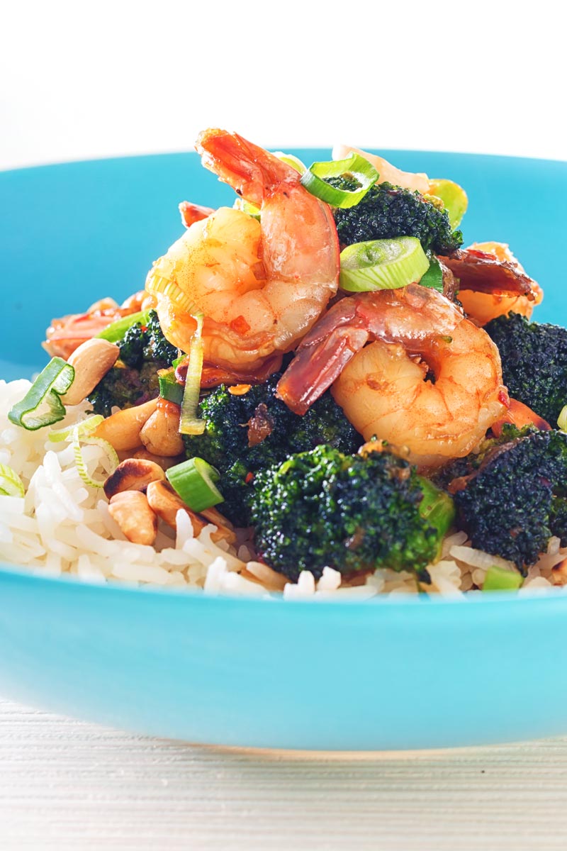 Close up tall image of teriyaki shrimp in a blue bowl with broccoli and white rice
