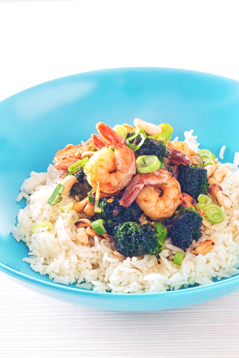 Tall image of teriyaki shrimp in a blue bowl with broccoli and white rice