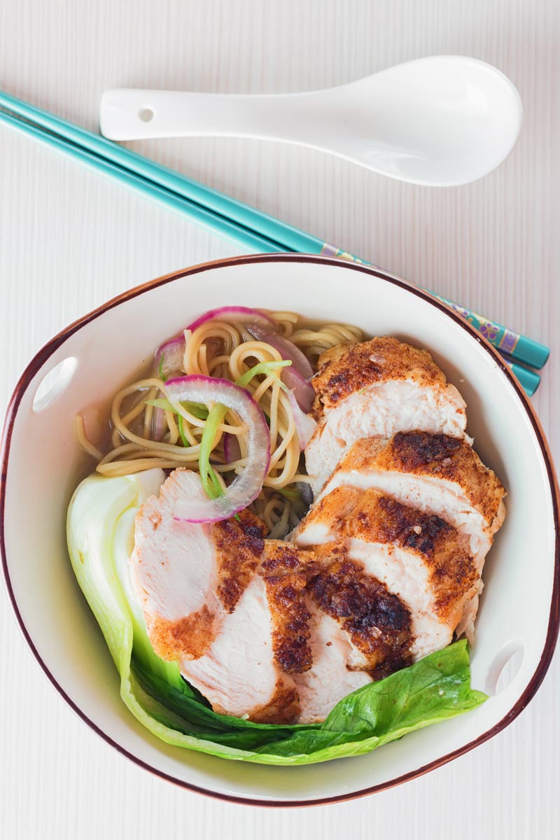 Tall image taken from above of a Chinese chicken noodle soup featuring with turquoise chopsticks