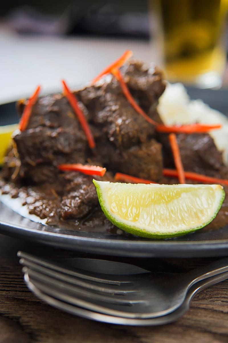 Close up portrait image of alime wedge served in front of an out of focus beef rendang with red chilli ribbons.