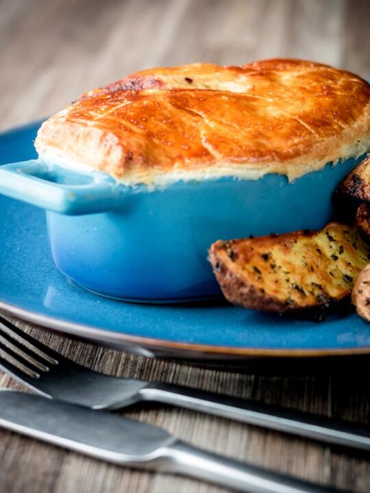 Square image of a Chicken and mushroom pie in a blue pot pie pot with potato wedges