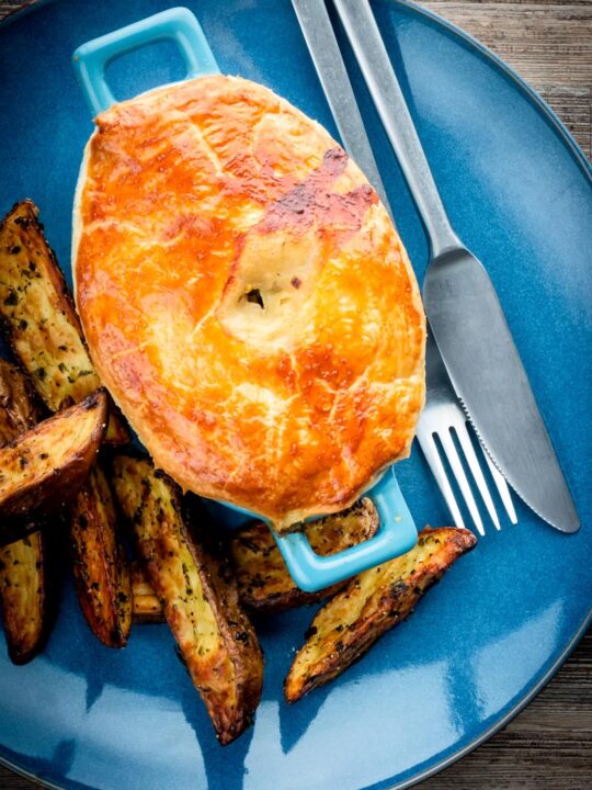 Portrait image of a Chicken and mushroom pie on a blue plate with potato wedges