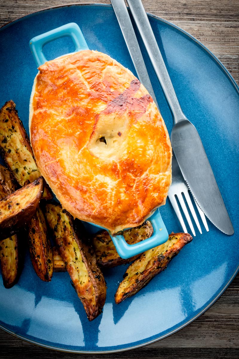 Portrait image of a Chicken and mushroom pie on a blue plate with potato wedges