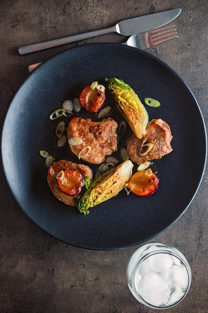 Chinese pork tenderloin with plums and seared lettuce served on a black plate