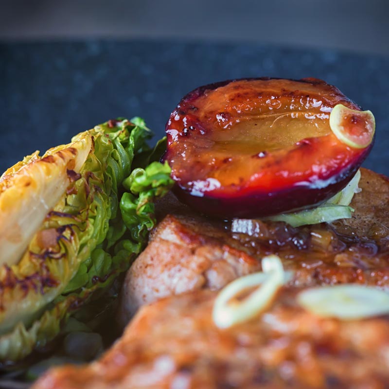 Close up image of pork with plums against a dark backdrop