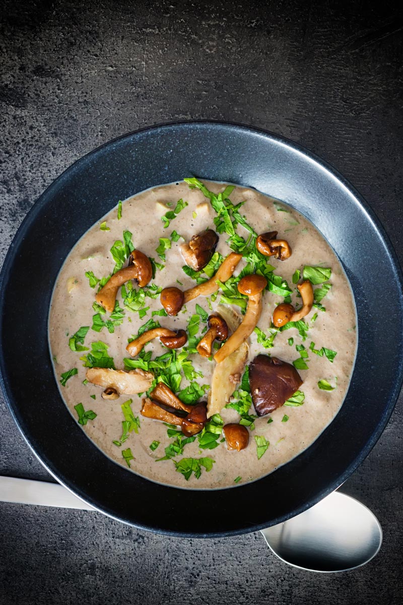 Over head portrait image of a bowl of cream of mushroom soup in a black bowl against a dark background