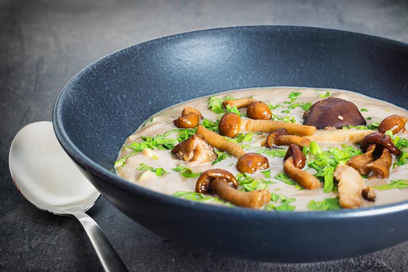 A bowl of cream of wild mushroom soup in a black bowl