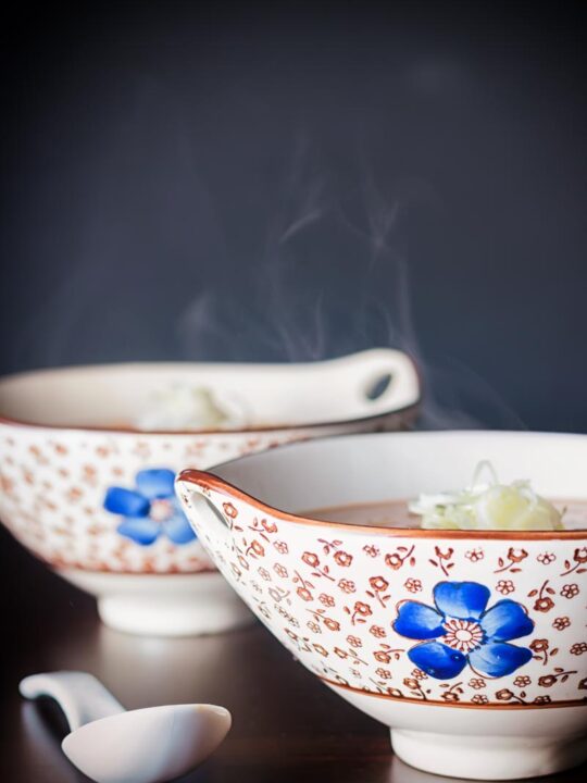 A steaming bowl of soup in an Asian soup bowl decorated with a blue flower