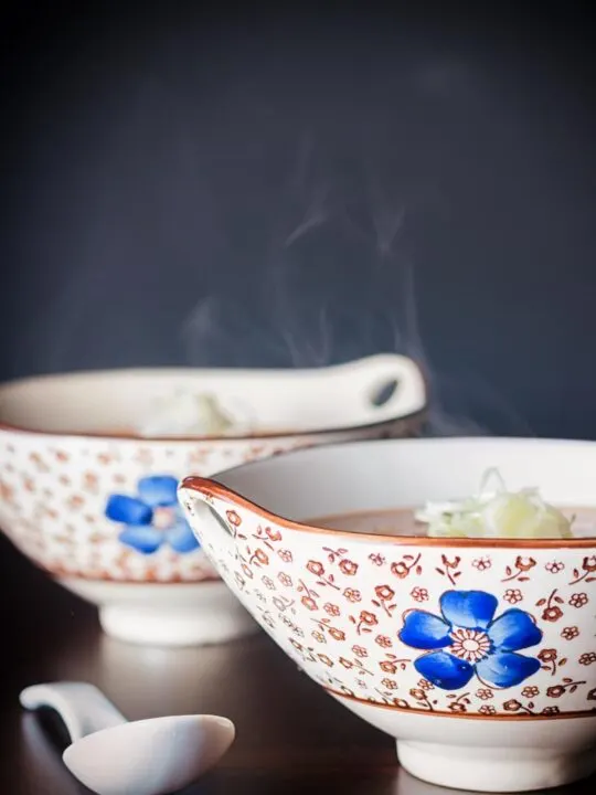 A steaming bowl of soup in an Asian soup bowl decorated with a blue flower