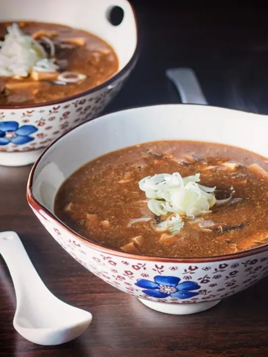 Square picture of hot and sour soup in an Asian style soup bowl and porcelain soup spoon