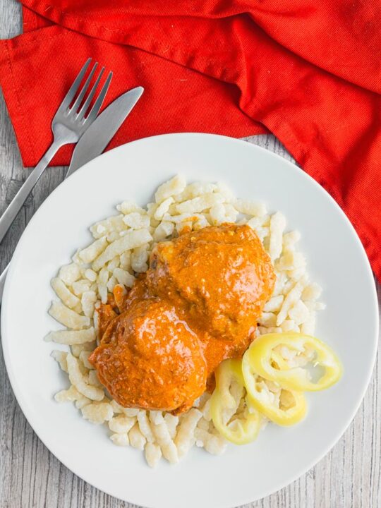Portrait image of Hungarian Chicken Paprikash cooked with chicken thighs on buttered nokedli on a white plate taken from above