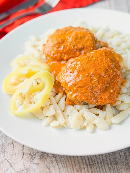 Portrait image of Hungarian Chicken Paprikash cooked with chicken thighs on buttered nokedli on a white plate