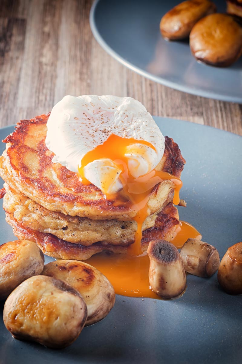 A perfectly poached egg with a dripping yolk sat on a stack of Irish boxty on a grey plate served with mushrooms