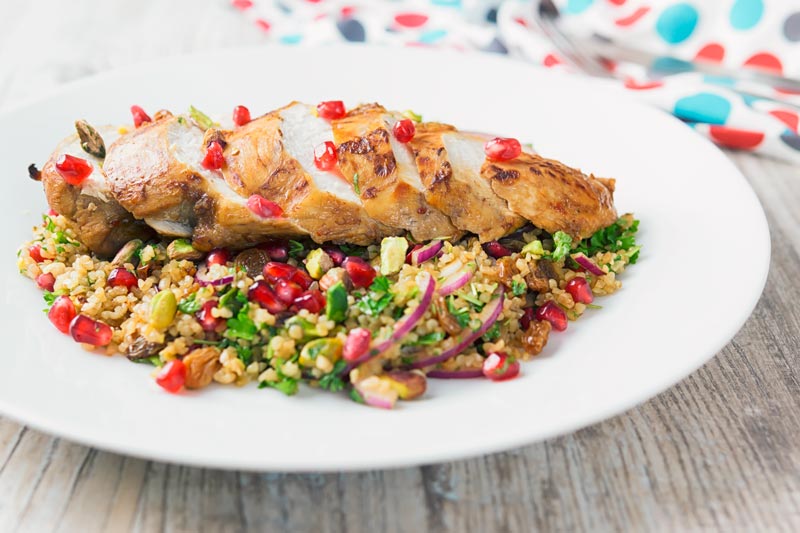 A sliced roasted pomegranate chicken breast on a bed of bulgur wheat salad