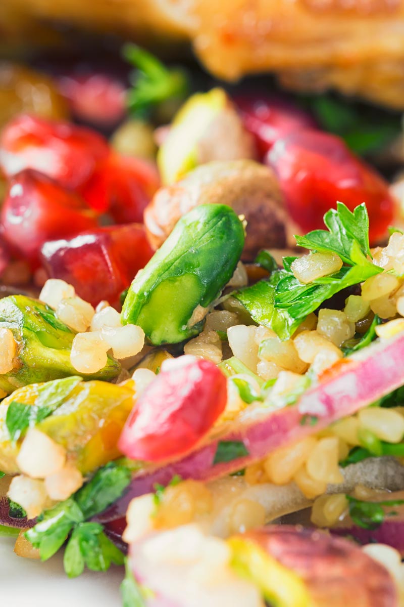 Close up image of a fruity bulgur wheat salad featuring pomegranate, red onion and pistachio nuts.