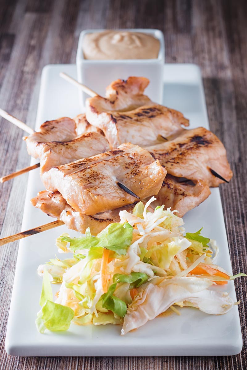 Tall image of pork satay with a side salad and peanut dipping sauce on a white plate
