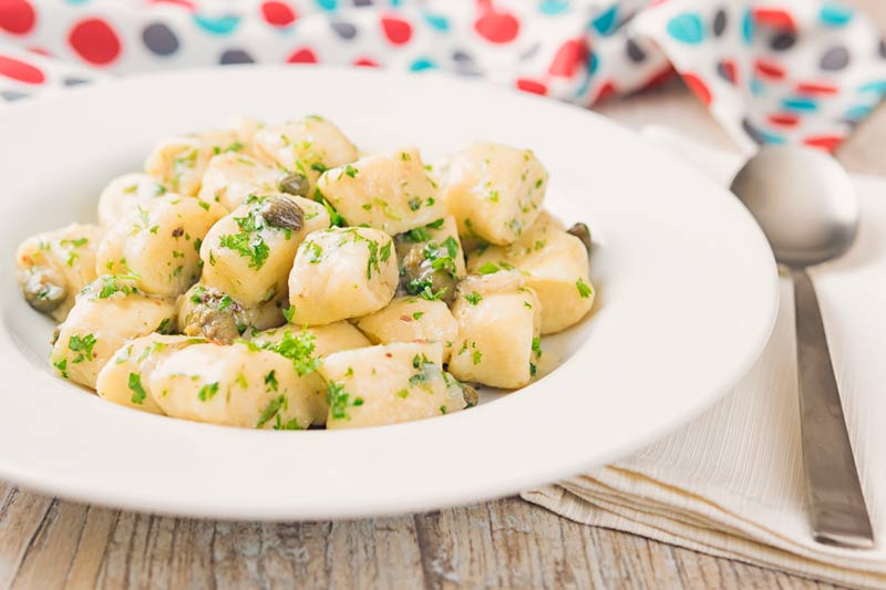 Landscape image of ricotta cheese gnocchi with capers and parsley in a white bowl