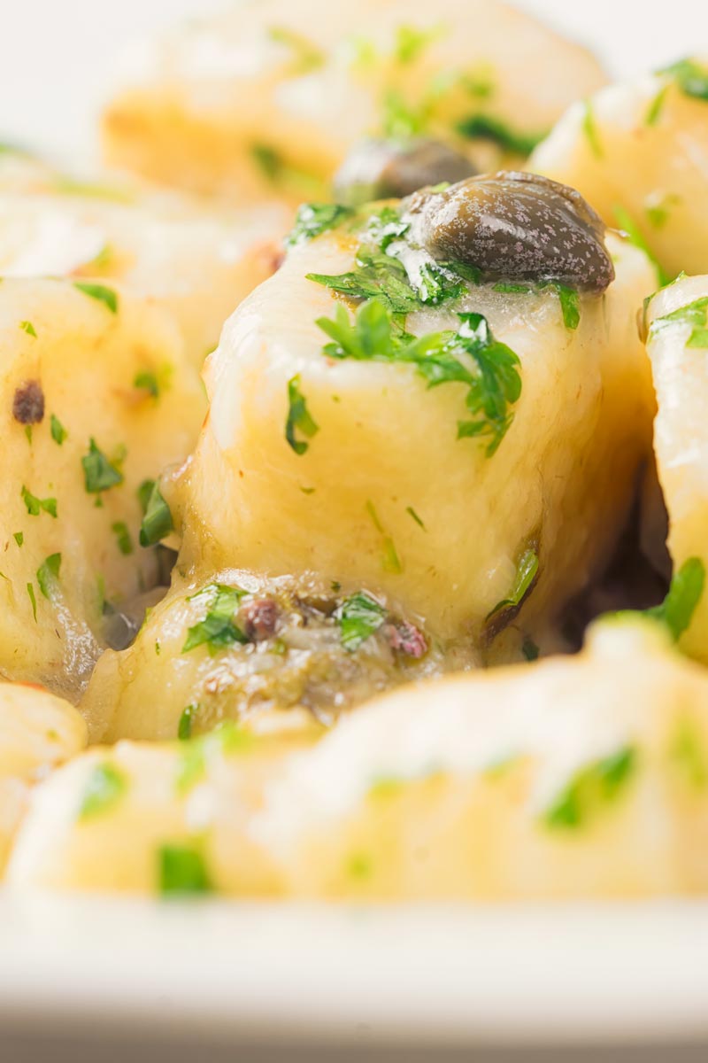Close up tall image of ricotta cheese gnocchi in a caper,parsley and butter sauce.