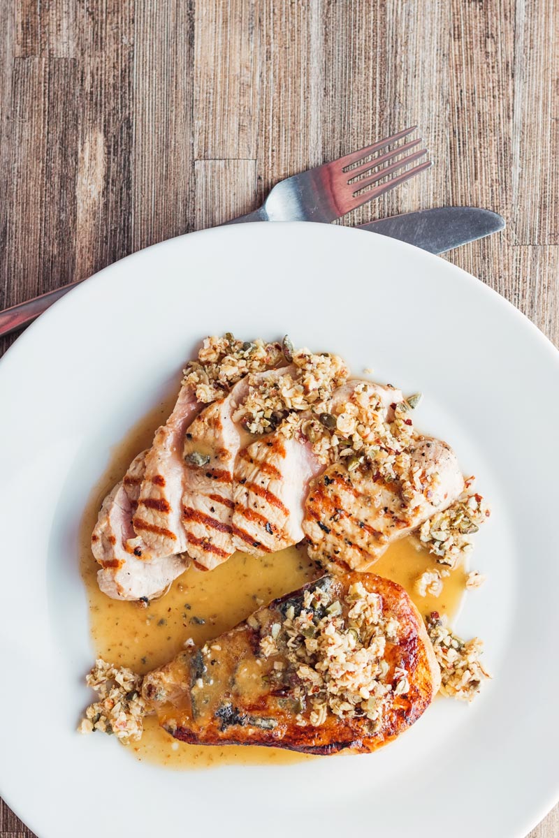 Tall image of roasted pears with blue cheese and a savoury crumble in a cider sauce and pork loin steak on a white plate