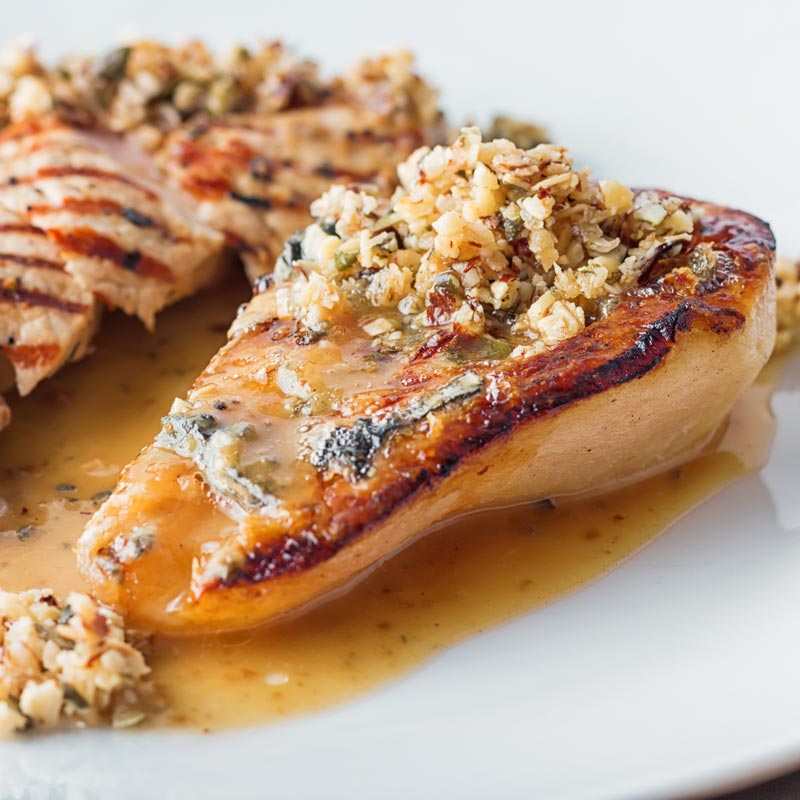 Close up square image of roasted pears with blue cheese and a savoury crumble in a cider sauce