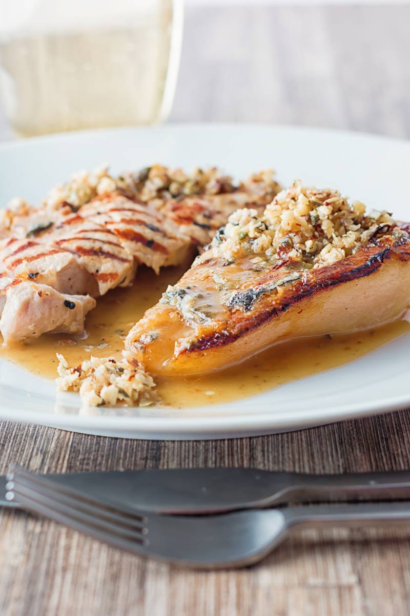 Tall image of roasted pears with blue cheese and a savoury crumble in a cider sauce on a white plate