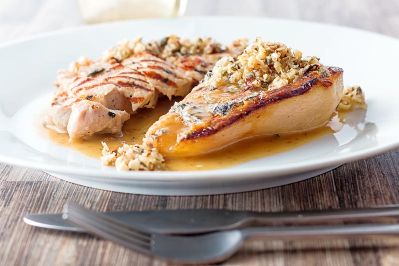 Landscape image of roasted pears with blue cheese and a savoury crumble and pork loin steak in a cider sauce on a white plate