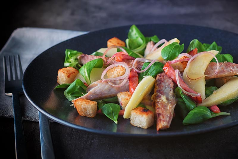 Landscape image of smoked mackerel salad on a black plate