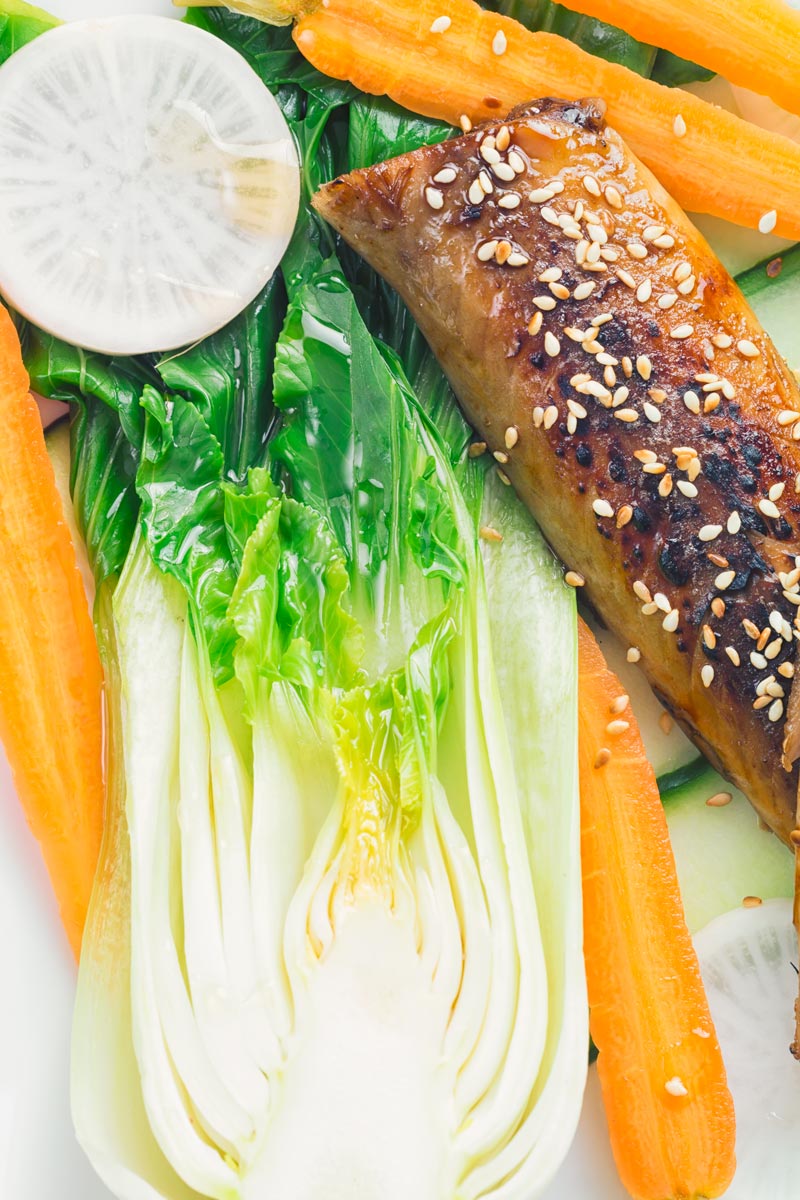 A broiled teriyaki smoked mackerel fillet with bok choi, white radish and pickled carrot close up