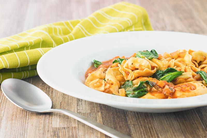 Landscape image of tortellini soup in a white bowl