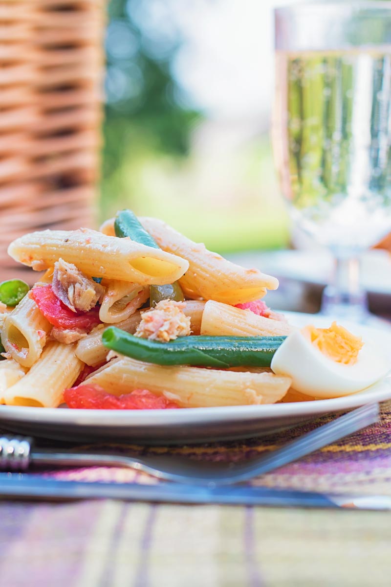 Tall image of a Tuna pasta salad in a picnic setting with a boiled egg