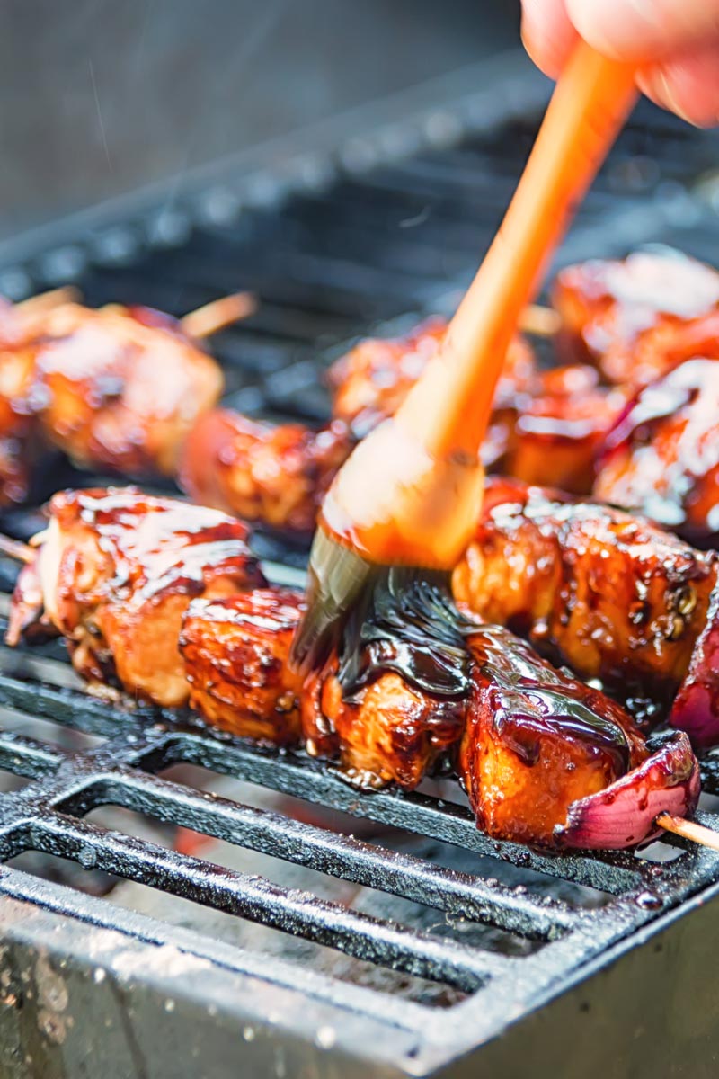 Pineapple chicken kebabs being coated in a bbq sauce cooking on a grill.